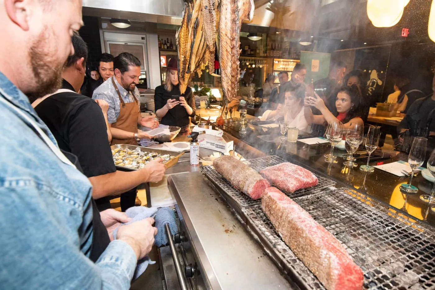 Chefs working a large open grill loaded with meat